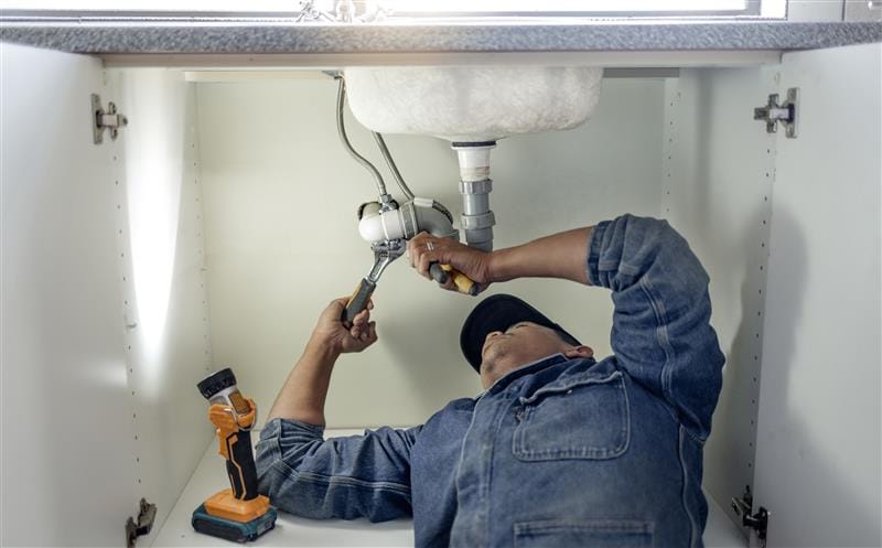 Plumber repairing pipes beneath a bathroom sink in San Dimas
